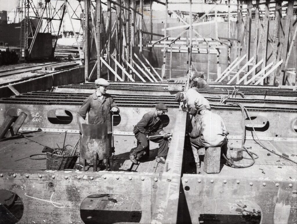 Fire mænd arbejder med at nitte jernplader på et skib